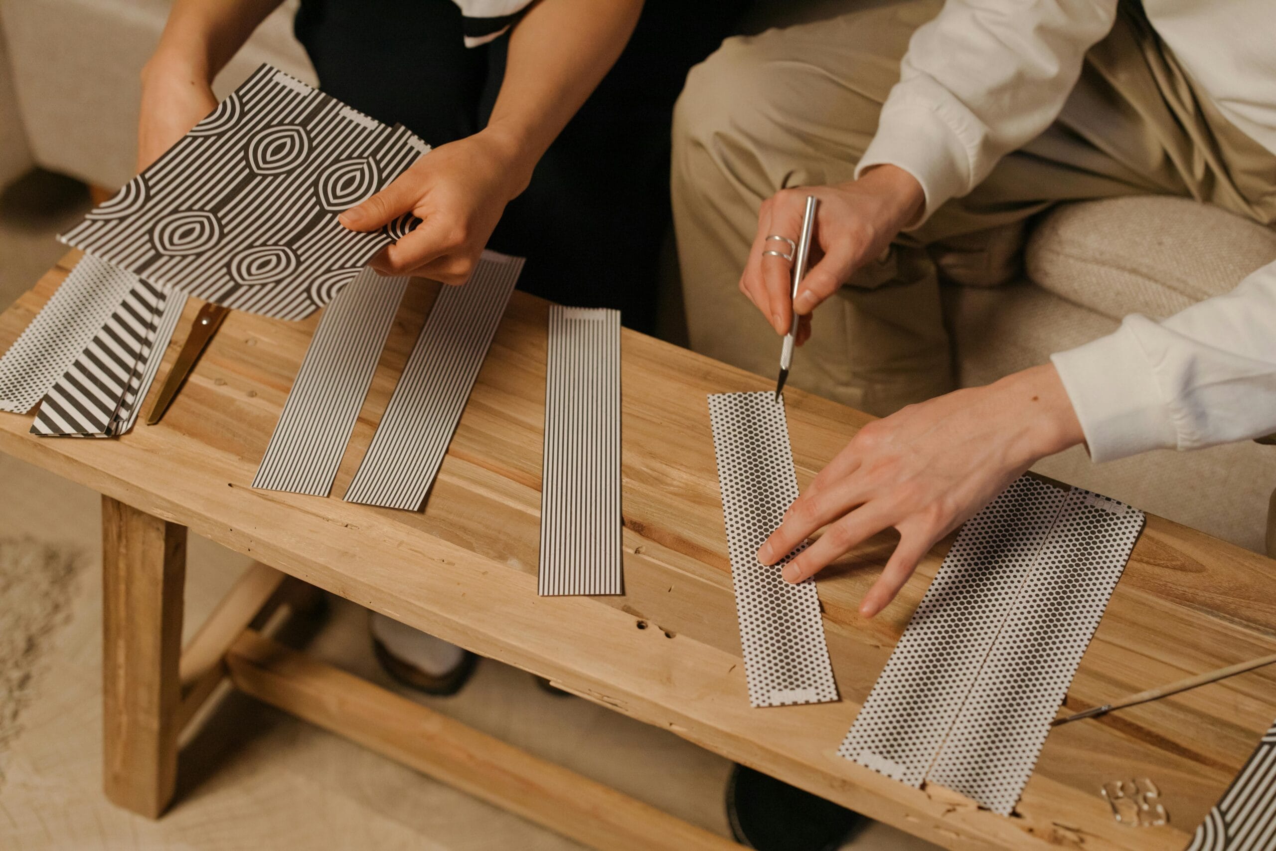 Two people crafting with black and white patterned paper on a wooden table.