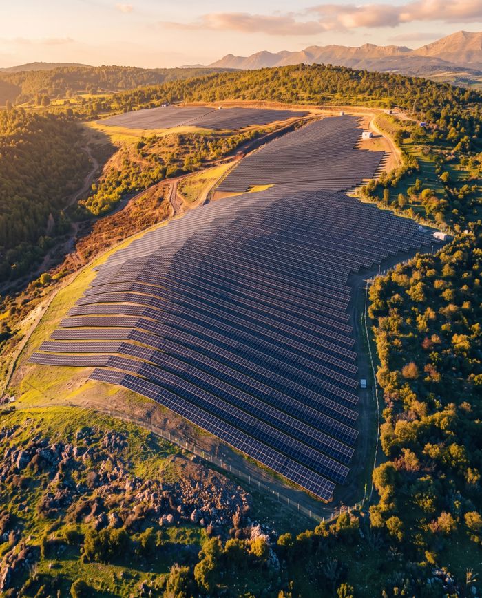 Aerial view of a vast solar panel installation amidst a hilly landscape under a beautiful sunset.